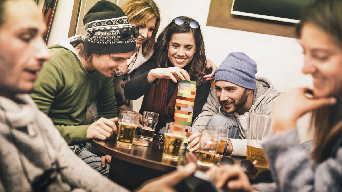 Un groupe de jeunes adultes jouent à un jeu de blocs colorés autour d'une table avec des verres de bière, dans une ambiance conviviale de bar à jeux.