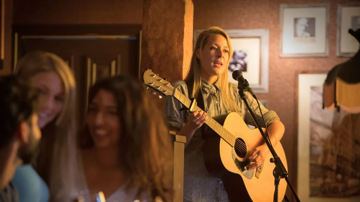 Musicienne jouant de la guitare acoustique au microphone dans un bar à Bordeaux, devant un petit public assis