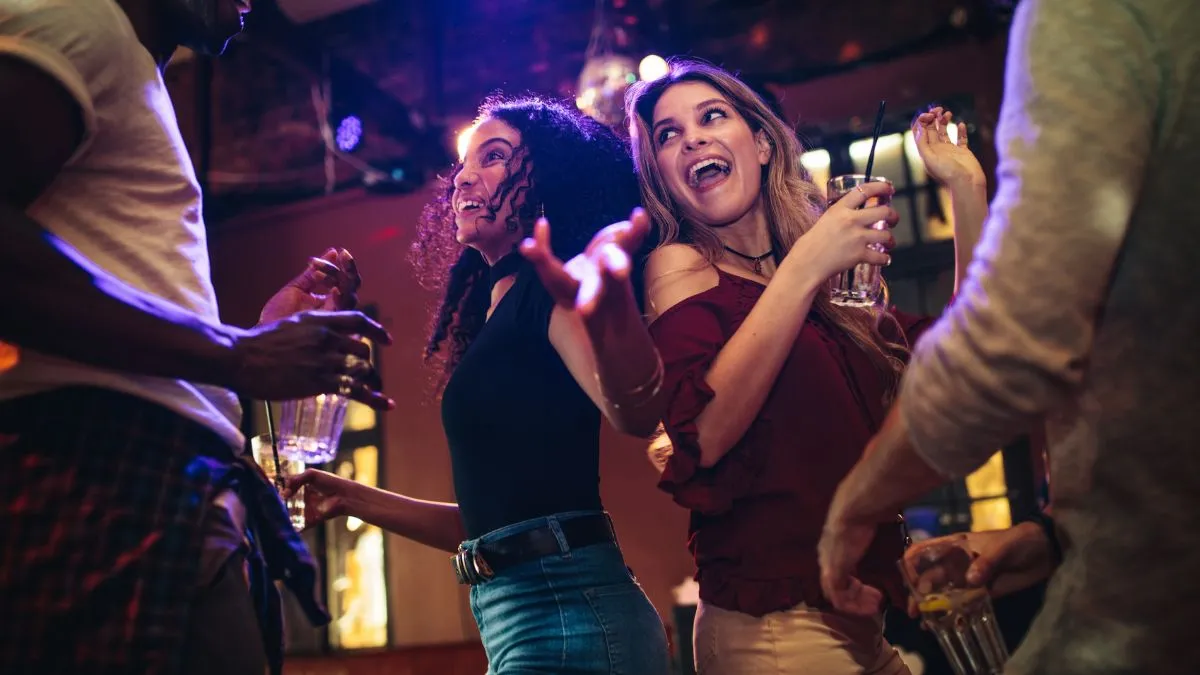 Groupe de jeunes adultes dansant et célébrant dans une discothèque avec éclairage bleu et violet, verre à la main