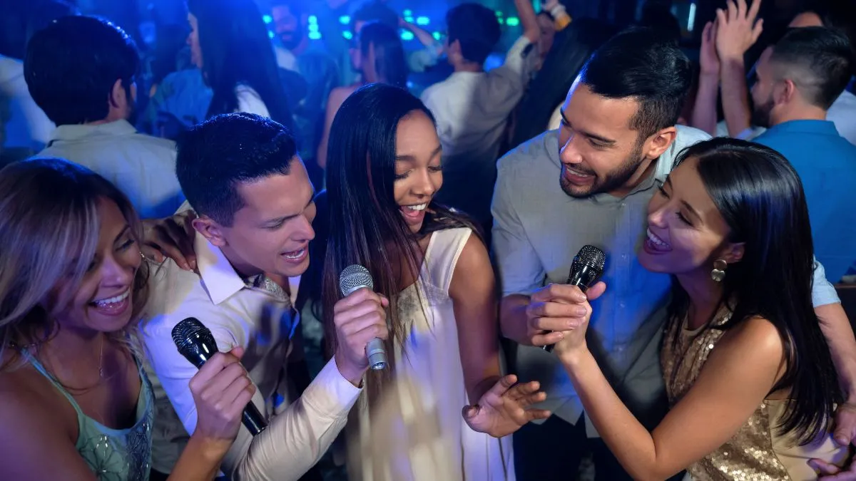 Groupe de jeunes adultes chantant au karaoké dans une discothèque avec éclairage bleu, tenant des microphones et s'amusant ensemble.