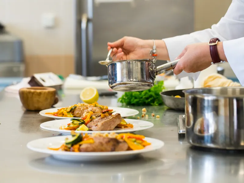 Chef versant une sauce depuis une casserole sur des assiettes de viande et légumes lors d'un atelier culinaire au Château Kirwan à Bordeaux