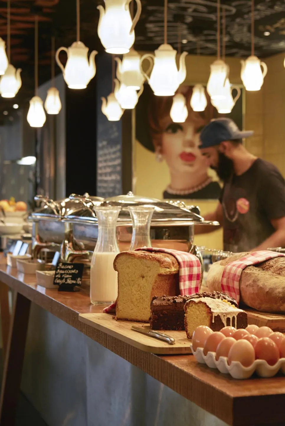 Comptoir du restaurant Mama Shelter à Bordeaux avec pains et pâtisseries artisanales, éclairage suspendu en porcelaine, et staff en arrière-plan