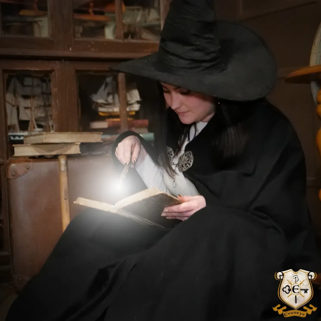 Femme vêtue de noir avec un chapeau de cowboy lisant un livre ouvert à la lumière, assise dans un cadre intérieur rustique à Bordeaux