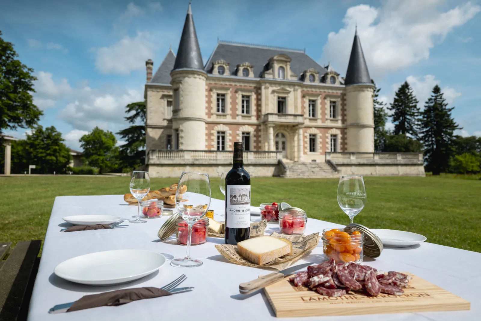 Table de pique-nique élégante dressée devant le Château Lamothe Bergeron à Bordeaux, avec verres de vin, charcuterie, fromage et bouteille de vin rouge