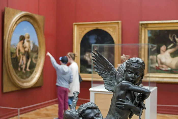 Intérieur du Musée des Beaux Arts de Bordeaux avec une sculpture d'ange en bronze au premier plan et une visiteure photographiant les peintures sur les murs rouges.