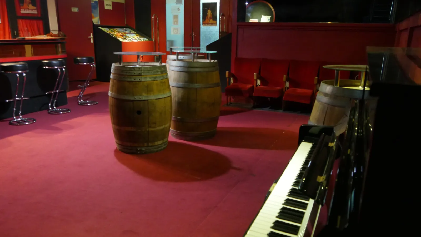 Intérieur du Théâtre du Pont Tournant de Bordeaux avec des tonneaux de vin, un piano à queue noir et des chaises rouges sur fond de murs rouges.