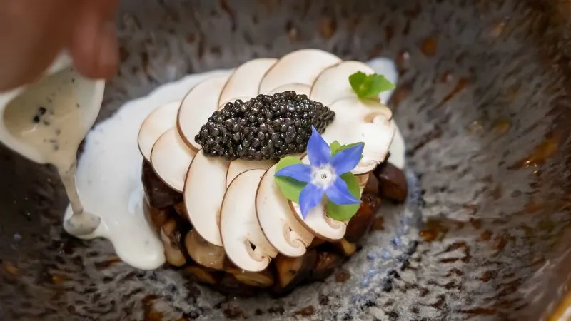 Assiette gastronomique du restaurant Passage Secret à Bordeaux présentant un toast garni de tranches de foie gras, de caviar noir et décoré d'une fleur bleue comestible sur fond de pierre grise