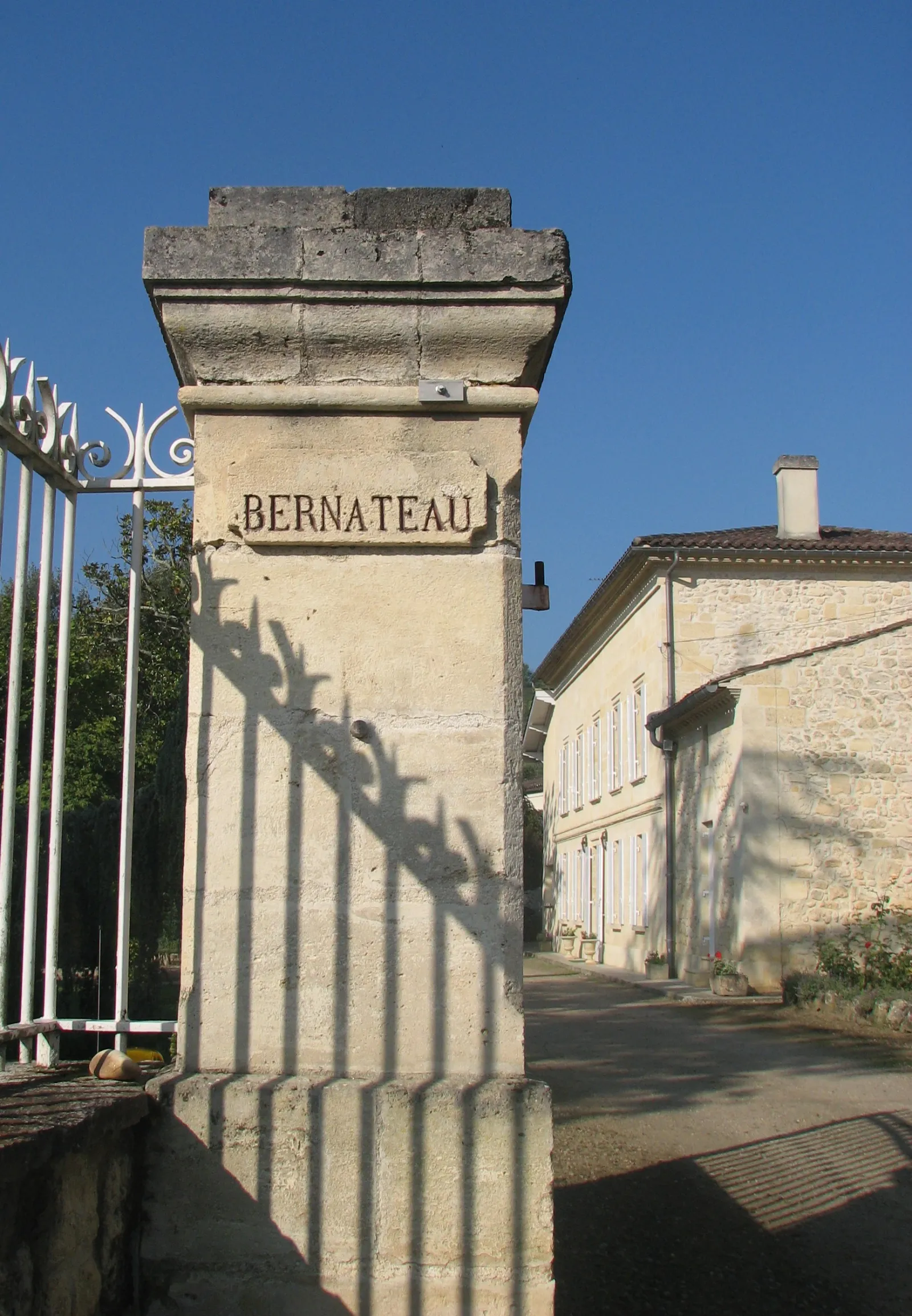 Pilier d'entrée du Château Bernateau à Bordeaux avec inscription du nom, portail blanc en arrière-plan et bâtisse en pierre sous ciel bleu