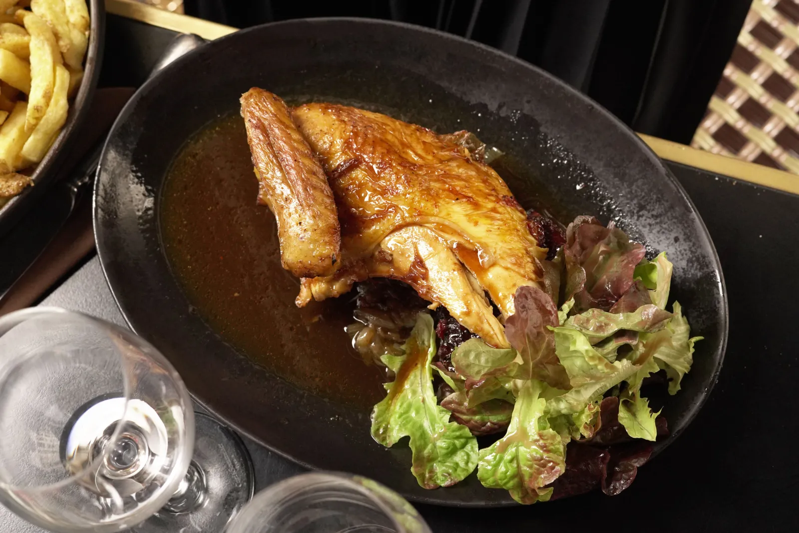 Canard rôti doré servi dans une assiette noire avec salade verte, accompagné de frites et d'un verre de vin blanc, dans un restaurant de Bordeaux