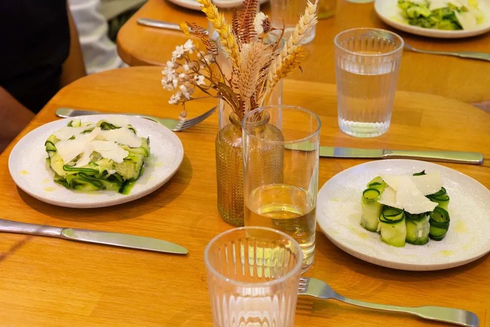 Table de restaurant avec deux assiettes de courgettes tranchées et fromage blanc, verres d'eau, décoration florale séchée, dans un cadre gastronomique bordelais.