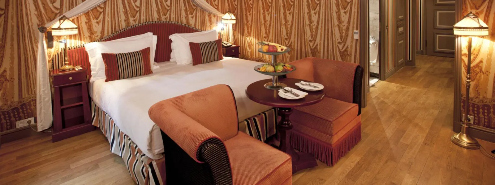 Suite luxueuse de l'Intercontinental Grand Hôtel de Bordeaux avec lit king-size, fauteuils orange, rideaux dorés et mobilier élégant
