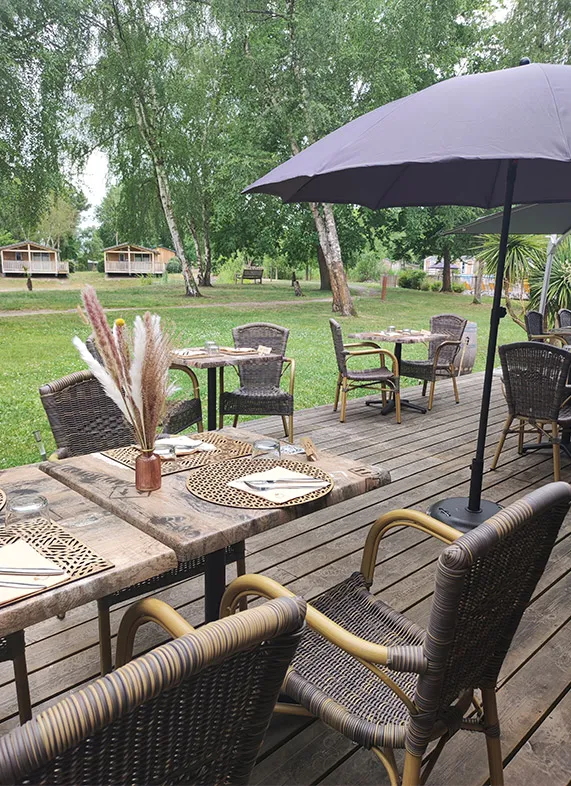 Terrasse extérieure du Bistrot du Lac à Bordeaux avec tables dressées, chaises en rotin, parasol noir, décoration florale et vue sur le parc verdoyant avec lac en arrière-plan
