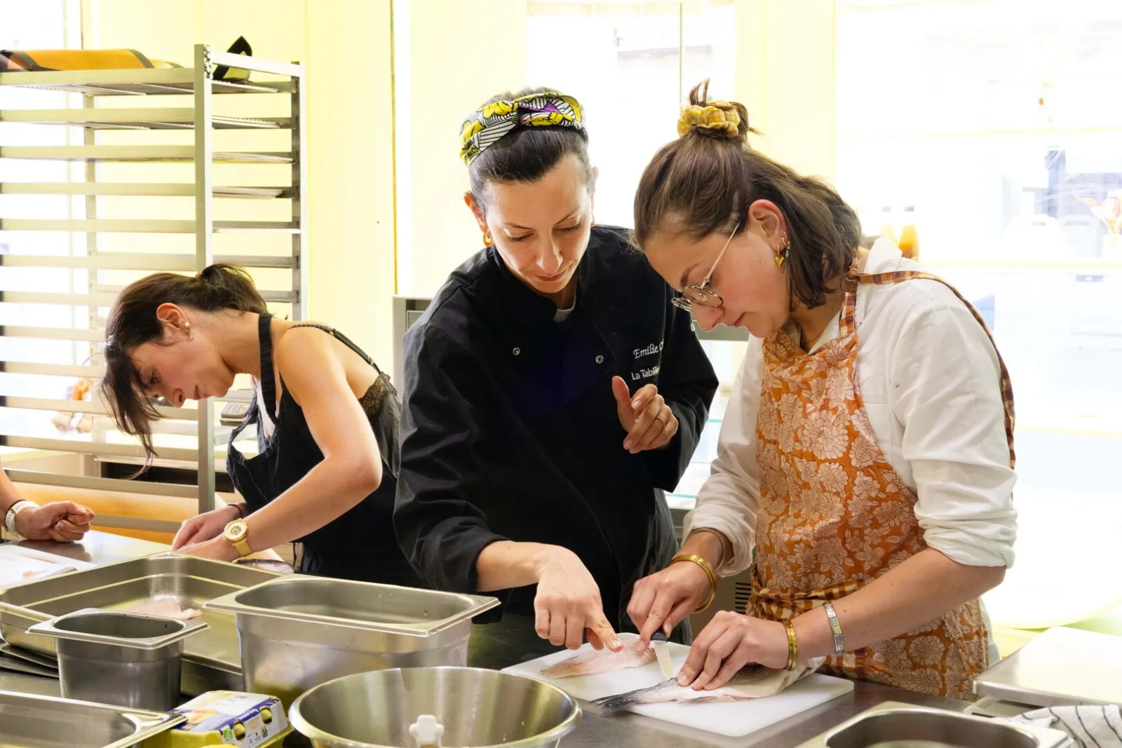 Trois femmes en cuisine préparent un plat dans un atelier culinaire à Bordeaux, l'une d'elles portant une veste de chef noir.