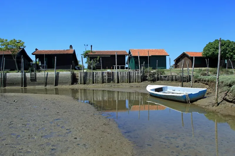 Cabanes de pêcheurs traditionelles sur pilotis avec un bateau bleu et blanc amarré dans le bassin à marée basse sur l'Île aux Oiseaux à Bordeaux