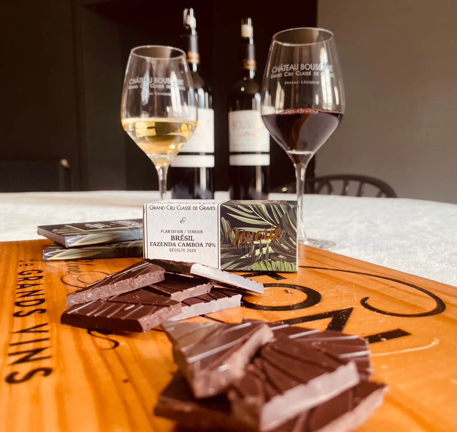 Dégustation de vins et chocolats au Château Bouscaut à Bordeaux : deux verres contenant un vin blanc et un vin rouge, accompagnés de chocolats artisanaux et d'une carte de présentation du cacao brésilien, sur une table orange.
