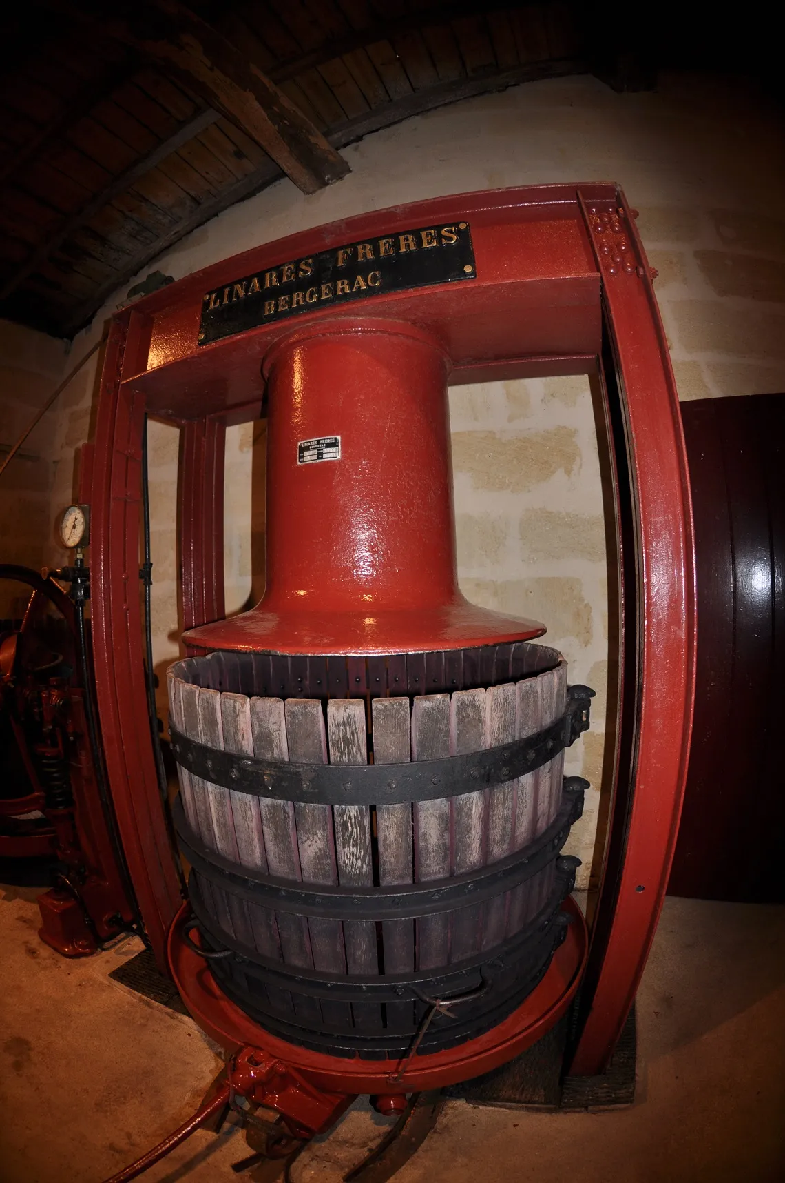 Ancien pressoir à raisin de couleur rouge de la maison Lindres Frères à Bergerac, exposé au Château Laniote à Bordeaux, avec un mécanisme de pression à vis central et des douelles en bois
