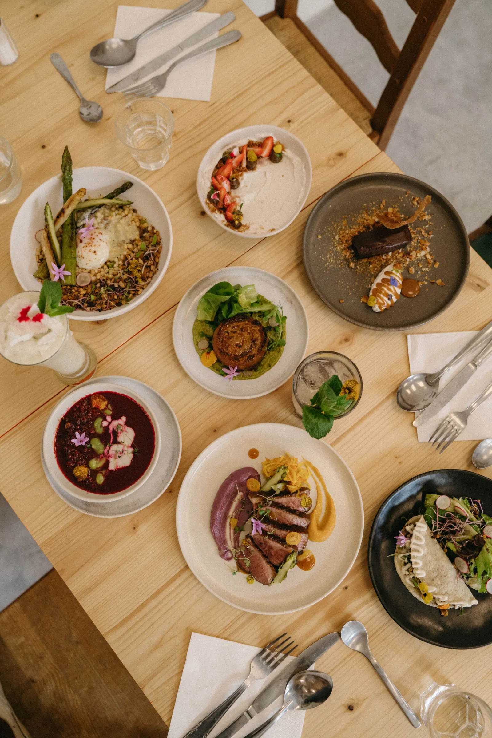 Vue de dessus d'une table de restaurant avec plusieurs assiettes de cuisine gastronomique : risotto aux asperges, viande rôtie, soupe betterave, poisson en croûte de sel, fruits de mer et légumes, présentés sur des assiettes blanches et noires avec décora