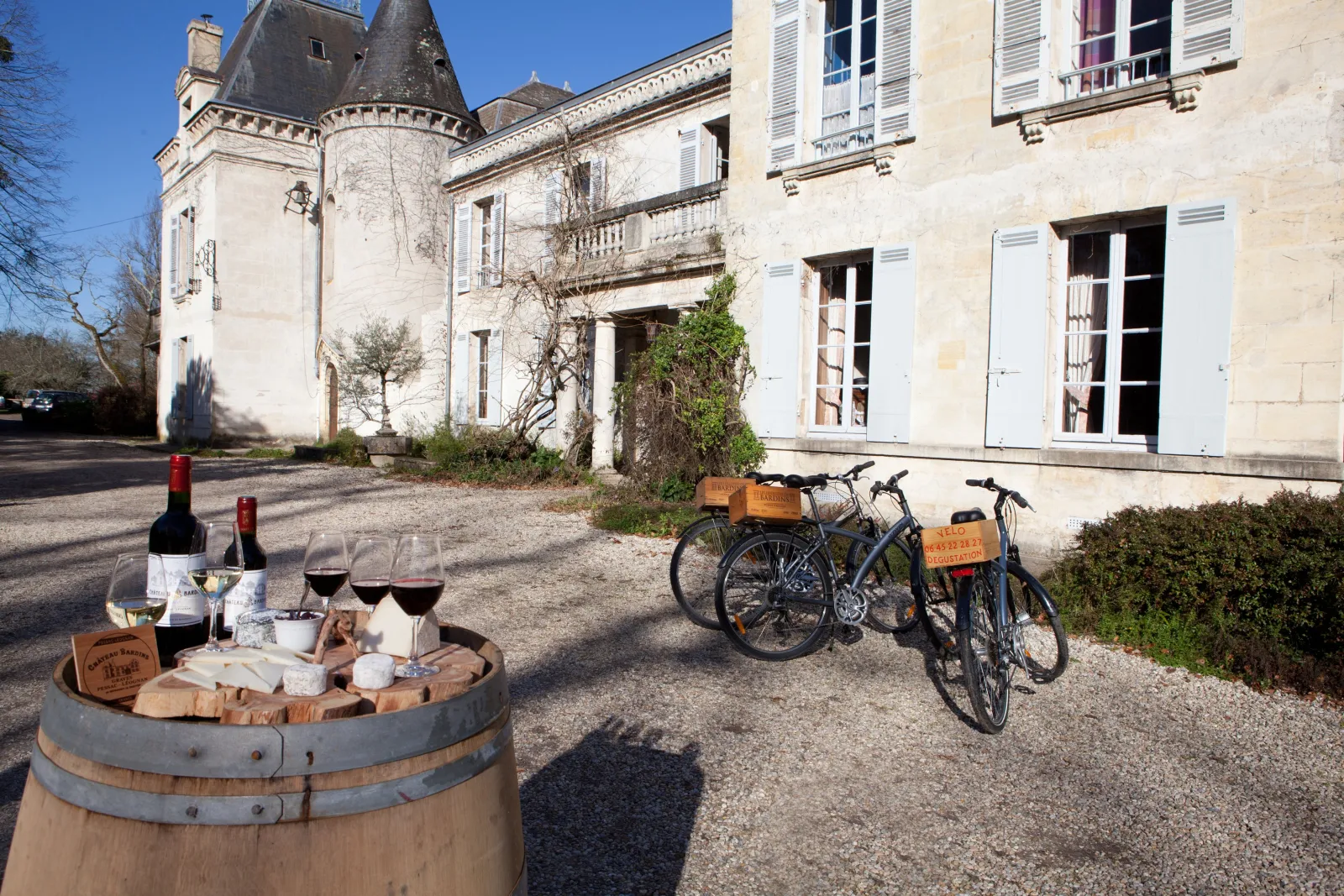 Dégustation de vin et plateau de fromage sur un fût de bois devant un château avec deux vélos garés dans la cour pavée