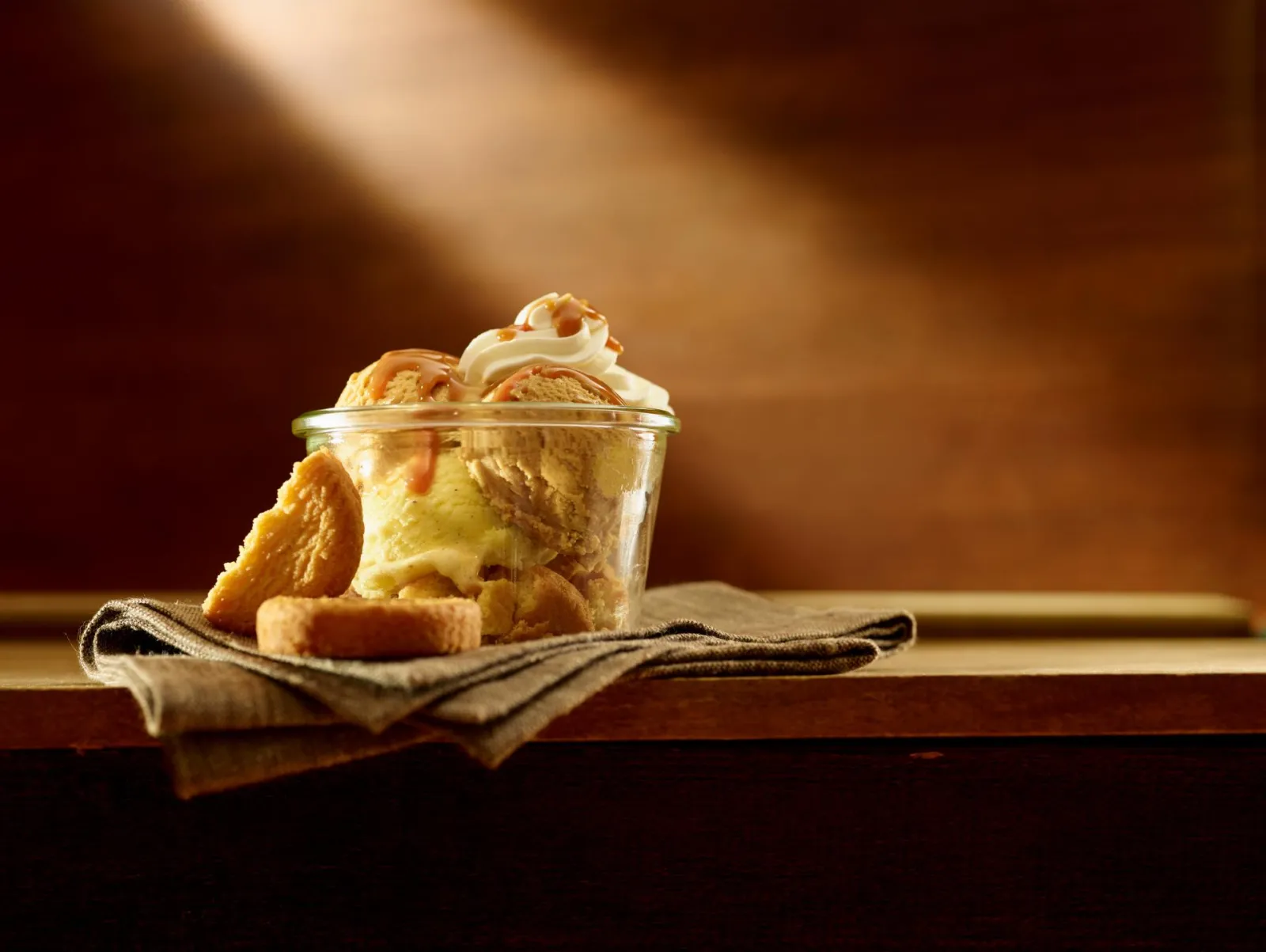 Verre de glace à la vanille avec crème fouettée et biscuit sec, présenté sur un linge beige dans une ambiance chaleureuse à Bordeaux