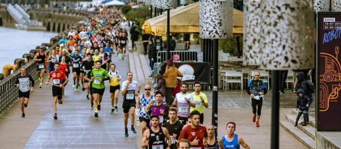 Des centaines de coureurs participent à une course de 10 km sur les quais de Bordeaux, portant des dossards de couleurs variées, avec la foule et les bâtiments historiques en arrière-plan.