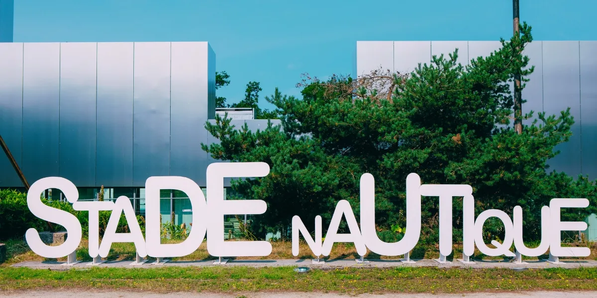 Enseigne blanche du Stade nautique Henri Deschamps devant un bâtiment moderne aux façades gris-bleu, à Bordeaux