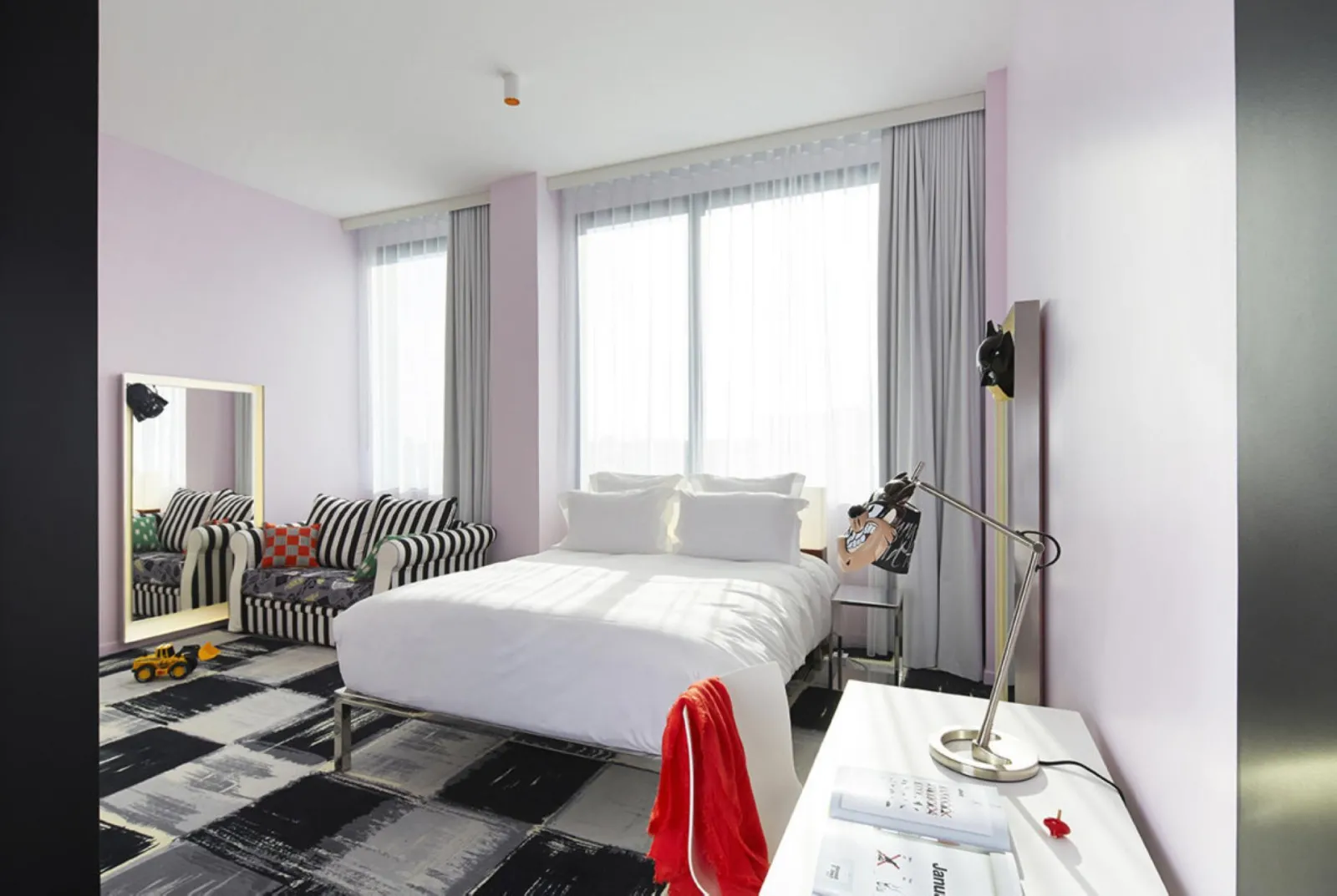 Chambre d'hôtel moderne et colorée au Mama Shelter de Bordeaux, avec lit blanc, fauteuils à rayures zèbres, murs rose pâle, grandes fenêtres avec rideaux gris et mobilier design contemporain.