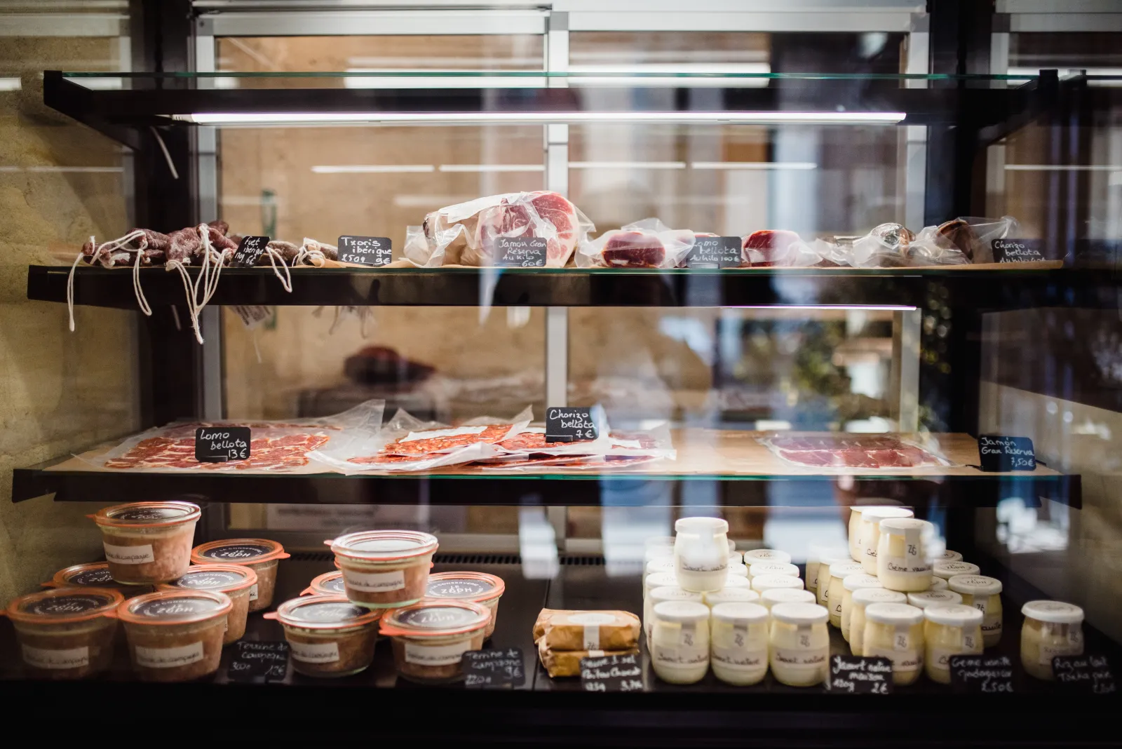 Vitrine de délicatessen avec charcuteries, fromages et produits gastronomiques français exposés sur trois niveaux de présentoir en verre à Bordeaux