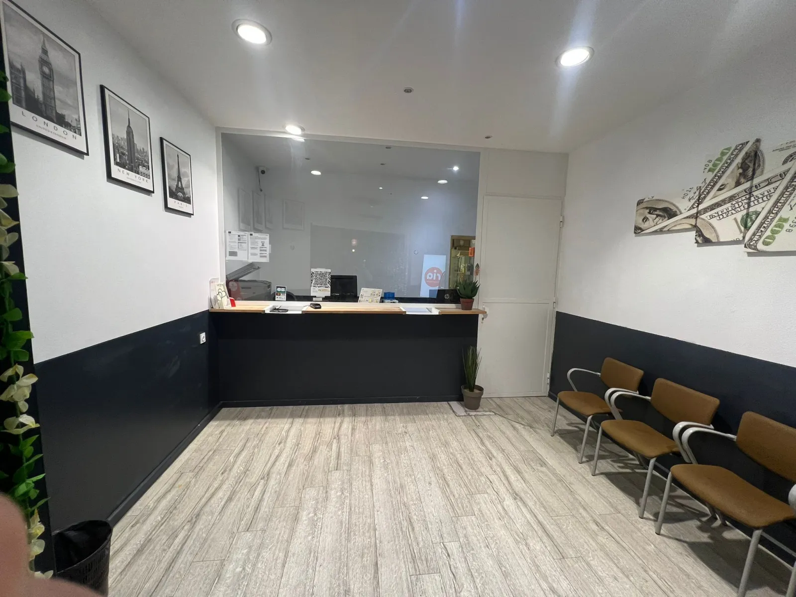 Réception moderne d'un bureau de change Monex à Bordeaux avec comptoir noir, chaises marron, sol gris clair, murs blanc et noir, et décoration murale incluant des photos de Big Ben et des billets de dollar.