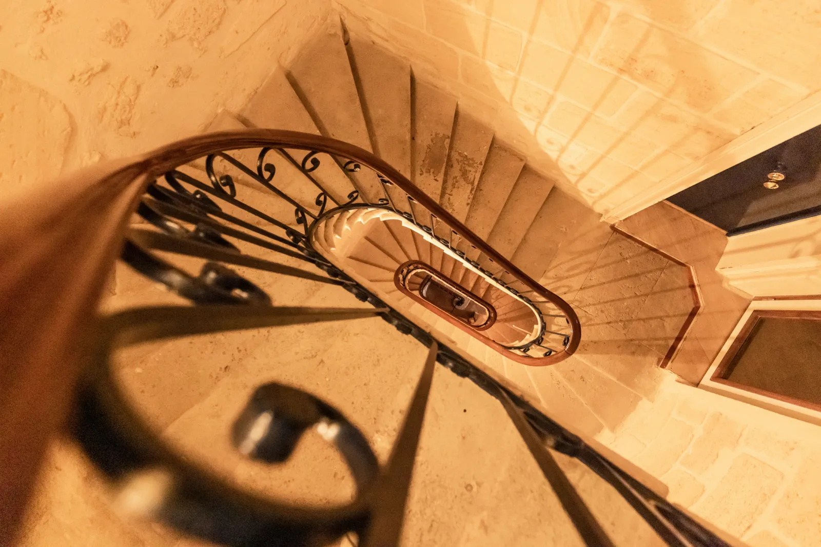 Vue en plongée d'un escalier en spirale avec rampe en fer forgé ornée, à l'intérieur de l'Hôtel de la Tour Intendance à Bordeaux