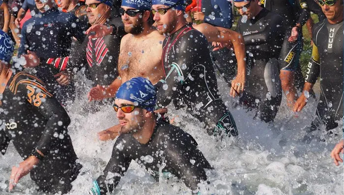 Groupe de triathlètes en sortie de l'eau lors du Triathlon de Bordeaux, éclaboussures d'eau visibles, nageurs équipés de combinaisons et lunettes de natation