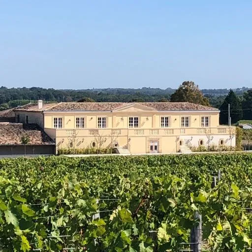 Château Larmande, un élégant bâtiment de pierre de couleur crème avec des rangées de fenêtres régulières, situé au cœur des vignobles de Bordeaux