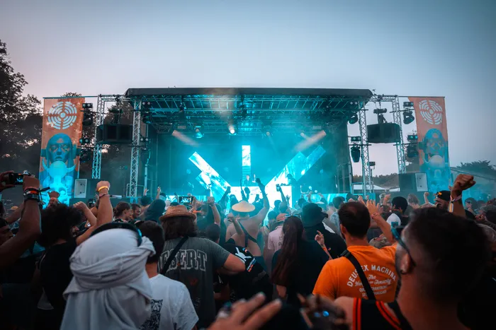 Foule de festivaliers devant une grande scène illuminée en bleu lors du festival Fort Décibel à Bordeaux, avec des mains levées et des téléphones pour filmer le spectacle.