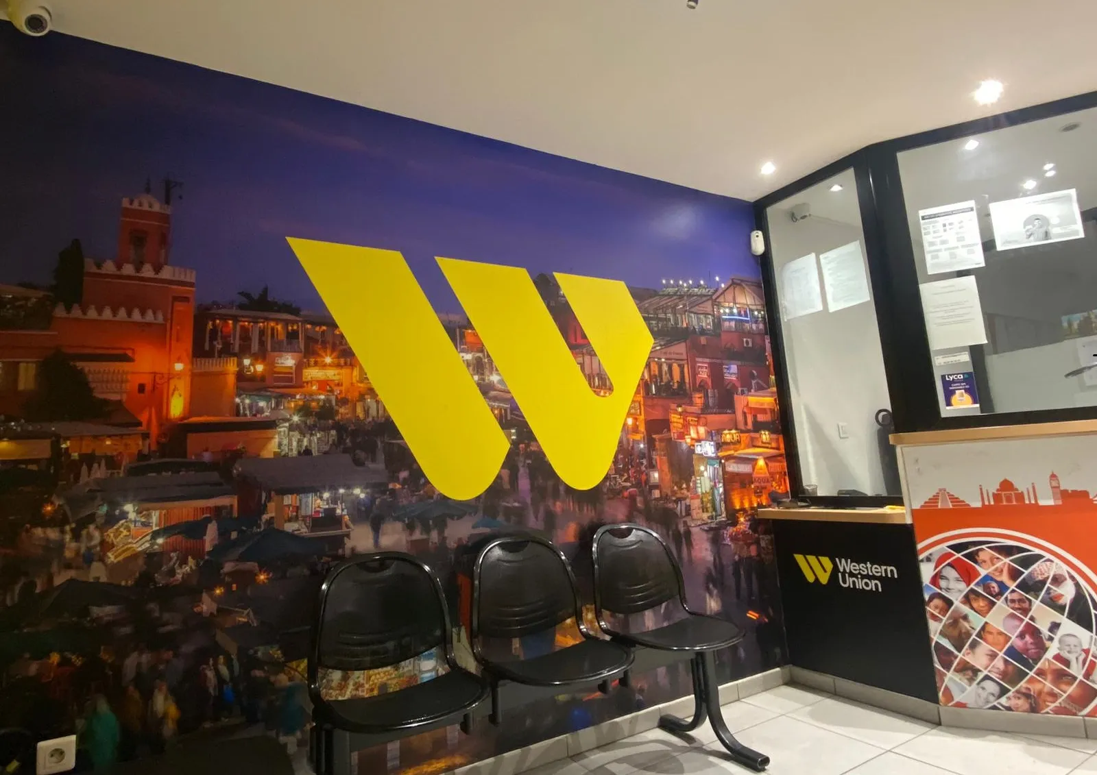 Agence Western Union à Bordeaux avec logo jaune géant sur mur de fond montrant la Place de la Bourse illuminée, chaises noires d'attente, et comptoir de service.