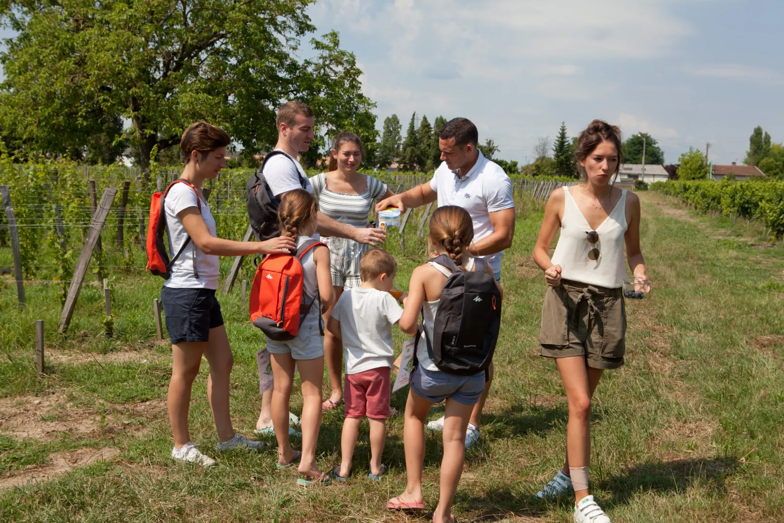 Un groupe d'adultes et d'enfants lors d'une visite guidée dans les vignes du Château, à Bordeaux, avec un animateur expliquant les pratiques viticoles.