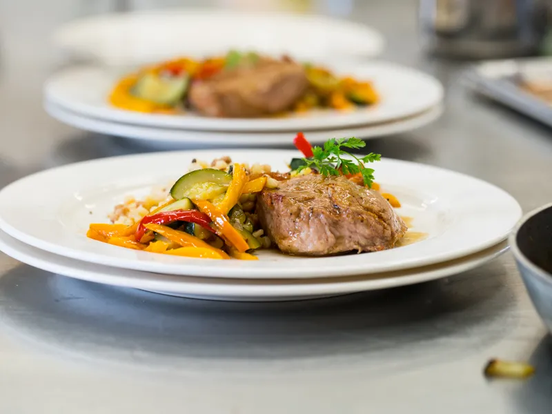 Assiette de viande grillée accompagnée de légumes sautés colorés et garnies de persil, présentée dans un atelier culinaire au Château Kirwan à Bordeaux.