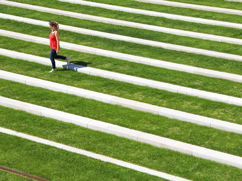Une femme en rouge court sur des marches blanches dans un parc avec pelouse verte à Bordeaux.
