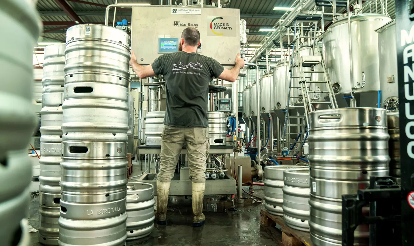 Un ouvrier manipule un équipement de brassage dans l'usine de bière Burdigala à Bordeaux, entouré de fûts métalliques de brassage alignés.