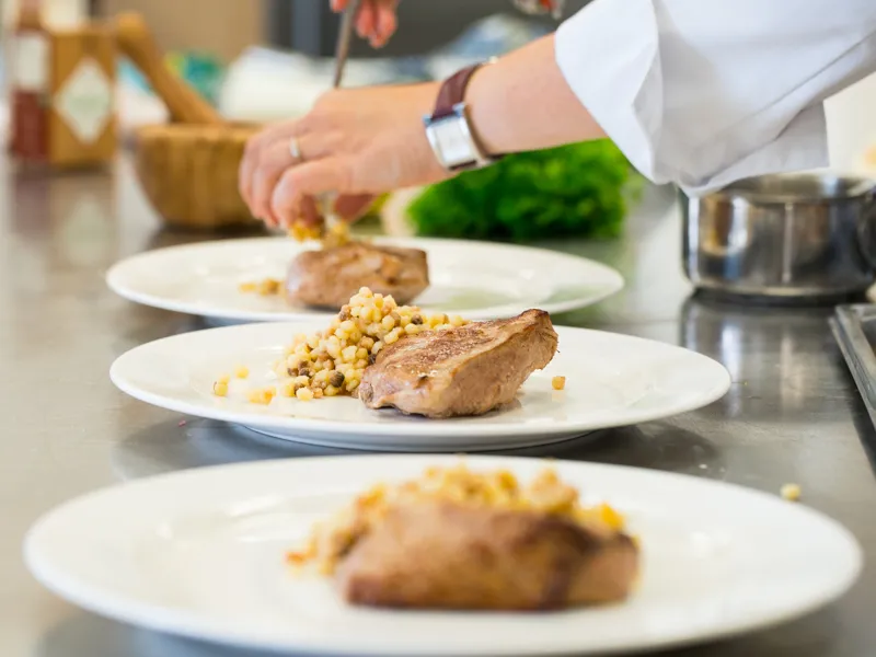 Un chef en cuisine prépare des assiettes avec du magret de canard et du maïs lors d'un atelier culinaire au Château Kirwan à Bordeaux.
