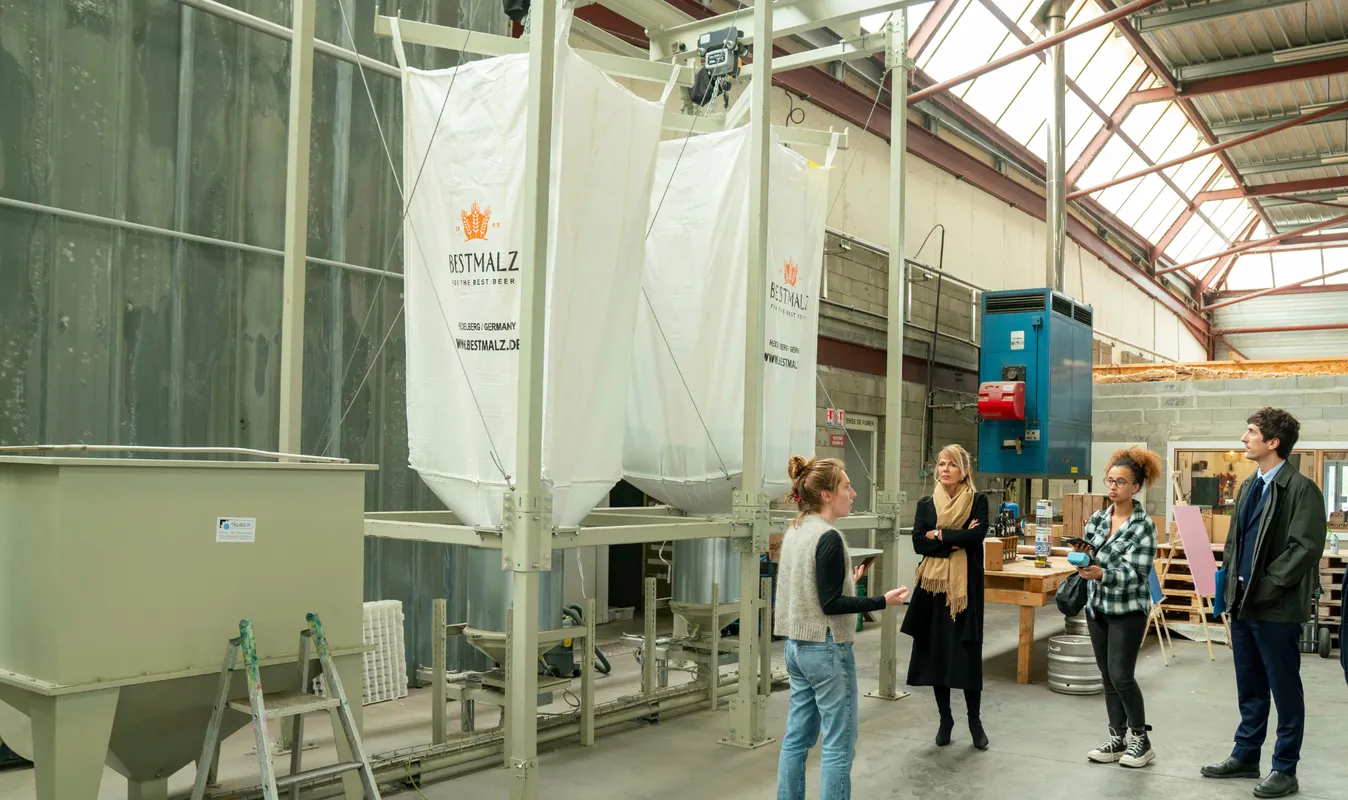 Visite guidée de la brasserie Bestmalz à Bordeaux avec des visiteurs observant les installations de brassage et les cuves de fermentation dans un hangar industriel.