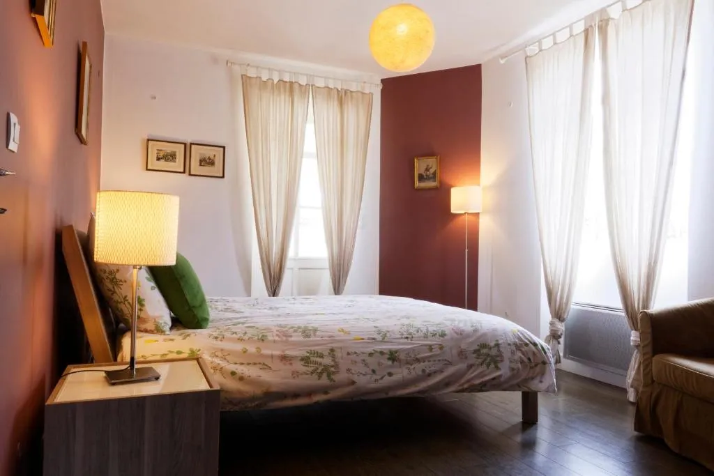 Chambre élégante à La Bastide de Siran, Bordeaux, avec lit double, murs terracotta et blancs, rideaux beige, lampes de chevet et luminaires modernes, fenêtres lumineuses et décoration soignée
