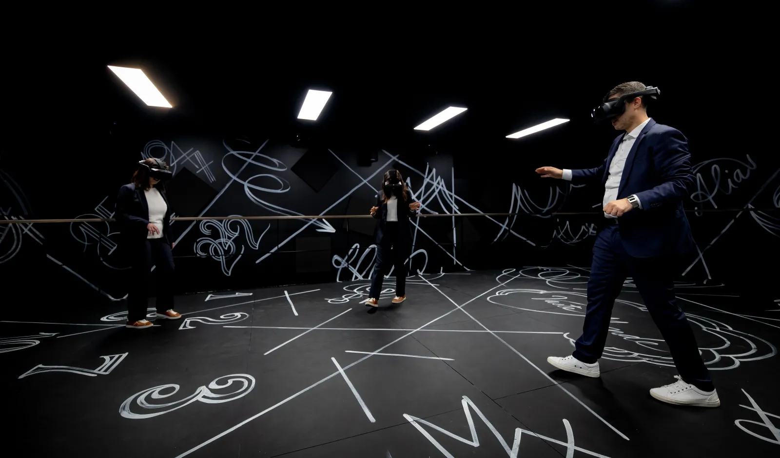 Visite immersive en réalité virtuelle à la maison Hennessy de Bordeaux, avec des visiteurs portant des casques VR dans un environnement futuriste aux murs noirs décorés de motifs abstraits blancs.