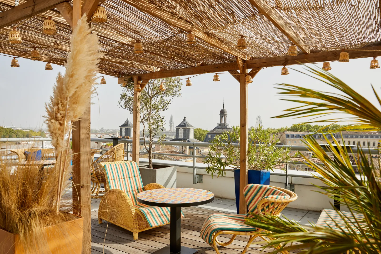 Terrasse panoramique à Bordeaux avec pergola en bois, chaises longues rayées, plantes décoratives et vue sur la basilique Saint-Michel et les toits de la ville