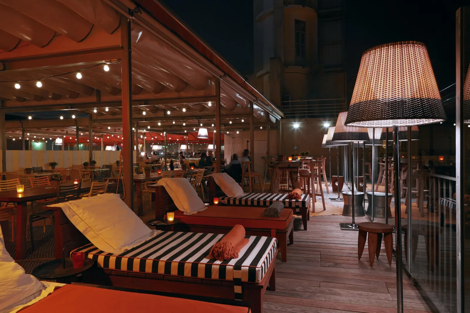 Terrasse de nuit du Mama Shelter Bar à Bordeaux avec transats rayés, lampadaires design et mobilier moderne illuminés
