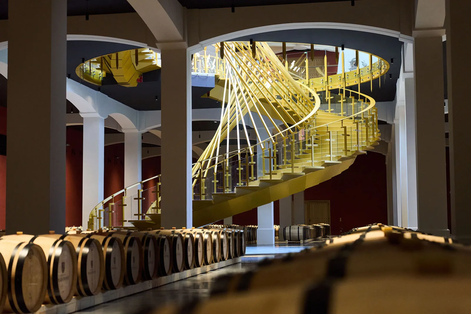 Escalier en spirale jaune vif dans une cave à vin avec tonneaux de chêne alignés au premier plan, château Plain Point à Bordeaux