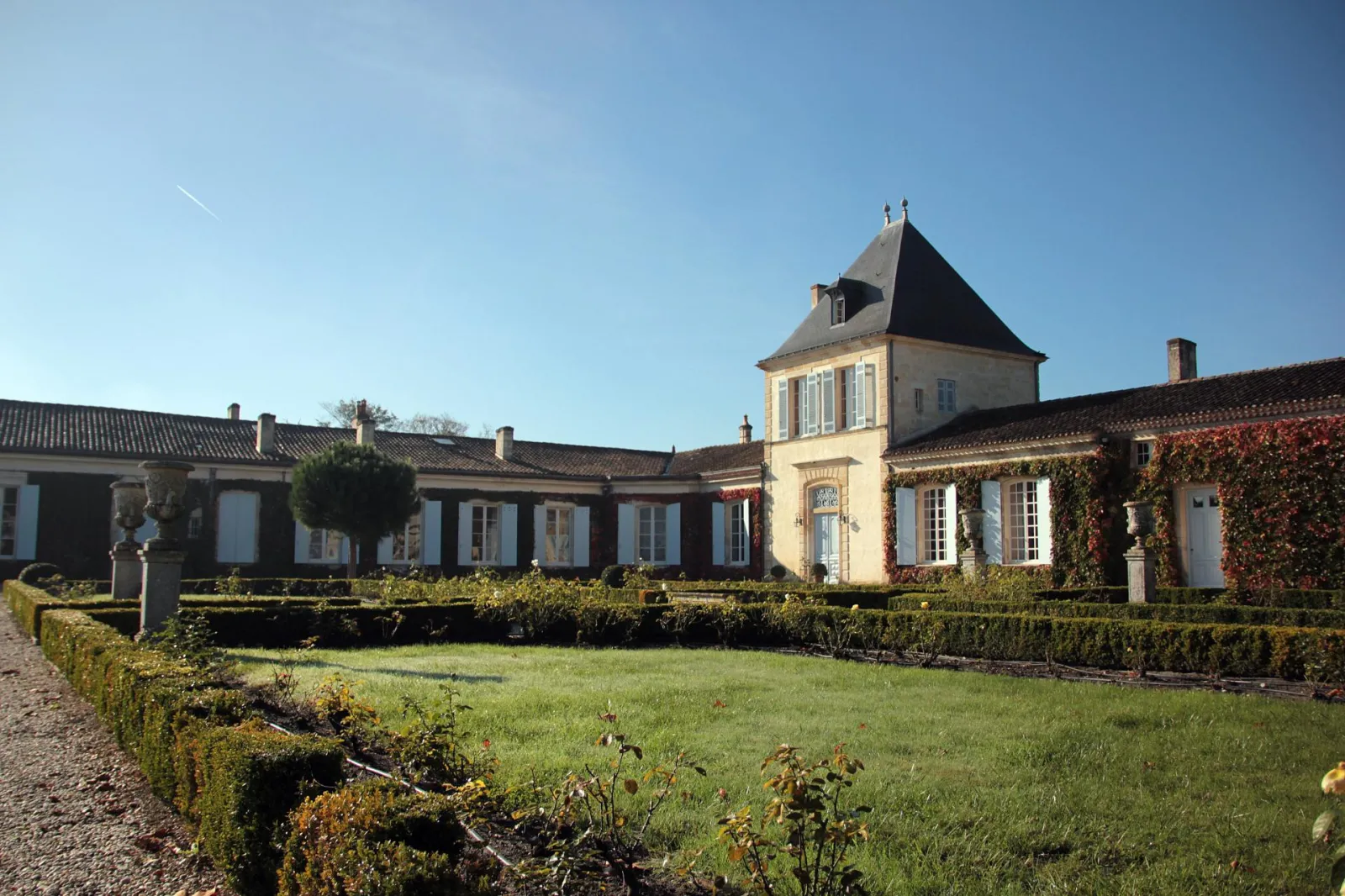 Château Paveil de Luze à Bordeaux, ensemble architectural avec tour mansardée, bâtiments aux volets bleus, cour intérieure paysagée avec haies et pelouse