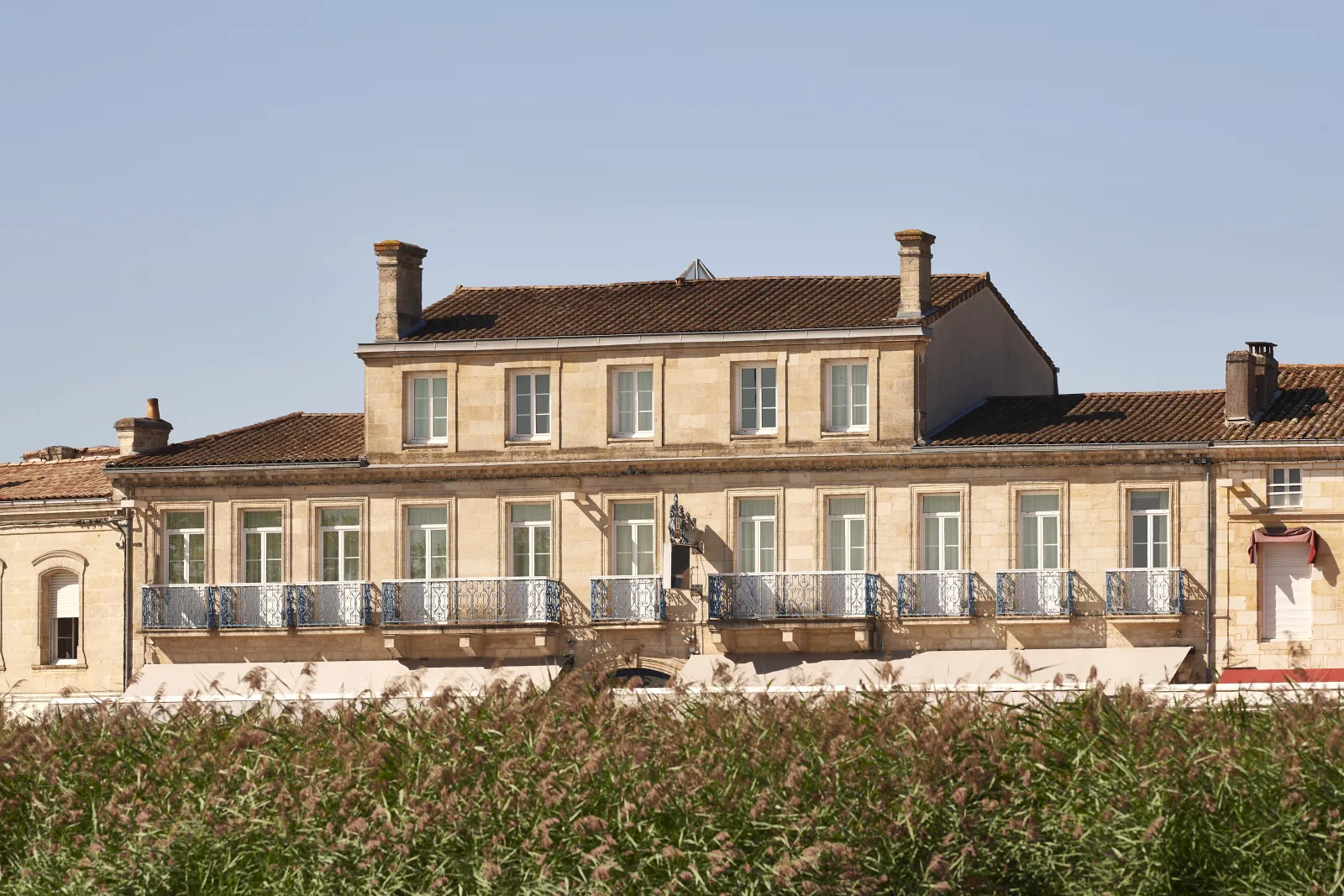 Façade élégante d'un bâtiment en pierre de taille avec balcon en fer forgé, surplombant un vignoble à Bordeaux