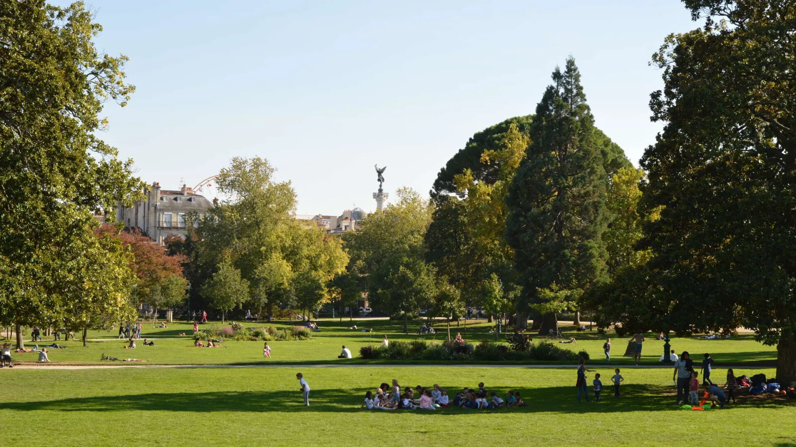 Bordeaux'nun Tarihi Parkı olan Jardin Public de Bordeaux'da güneşli bir günde yeşilliklerle çevrili tarihi anıtların önünde aileler ve ziyaretçiler
