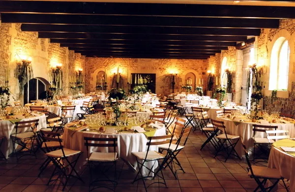 Salle de réception élégante du Château Lafitte à Bordeaux, décorée de tables rondes dressées avec nappes beiges, chaises noires, arrangements floraux et candélabres, illuminée par des appliques murales dorées.