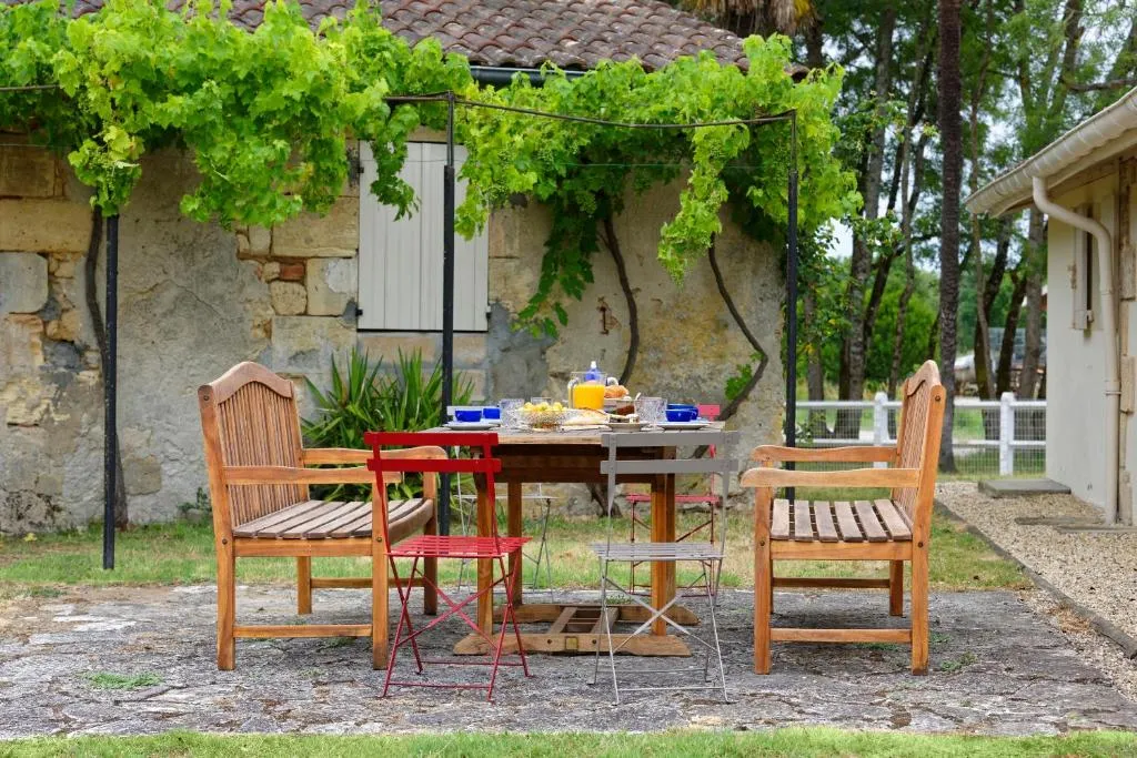 Terrasse aménagée avec table en bois, chaises longues en teck, pergola avec vigne vierge luxuriante, décoration de jardin rustique en pierre, à la Bastide de Siran près de Bordeaux