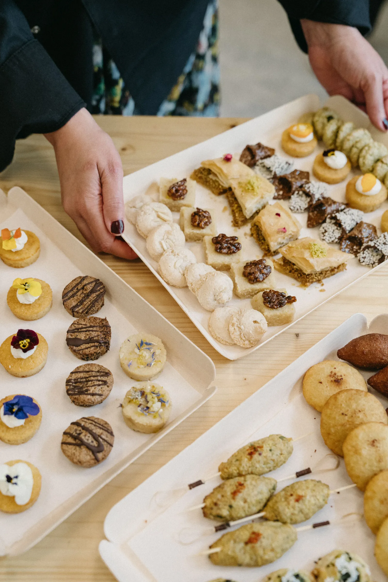 Assortiment de pâtisseries et biscuits décorés présentés sur des plateaux blancs dans un restaurant de Bordeaux, avec des mains qui arrangent les desserts
